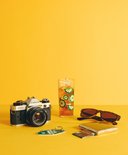 Camera, glass with a drink, sunglasses, and wallet on a yellow background