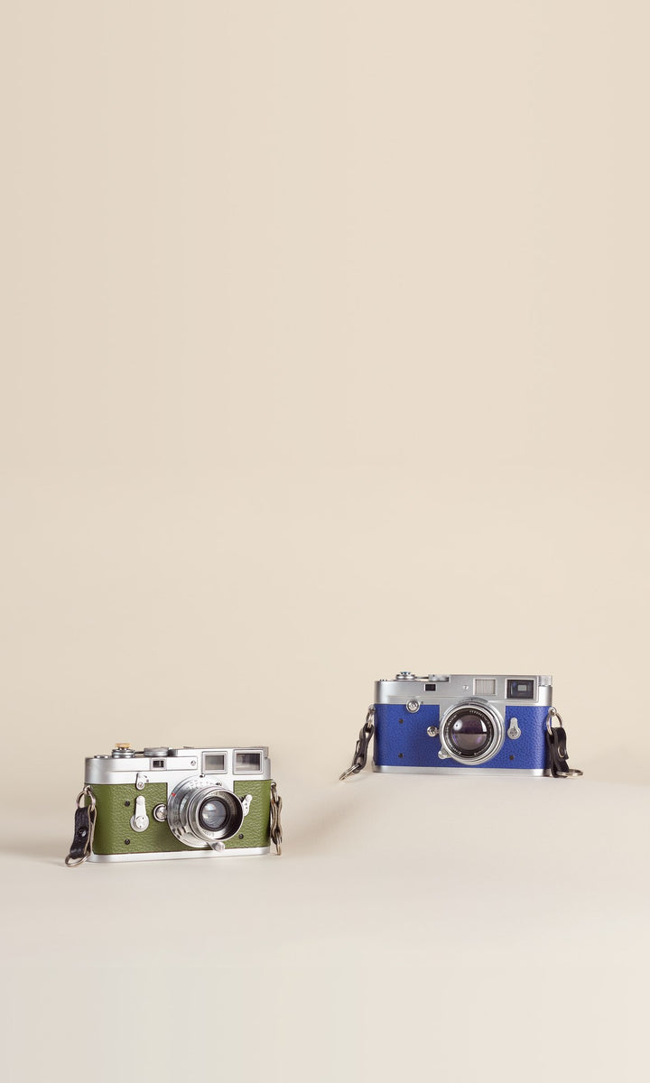 Restored Leica M3 in green leather and Leica M2 in blue leather on a cream backdrop