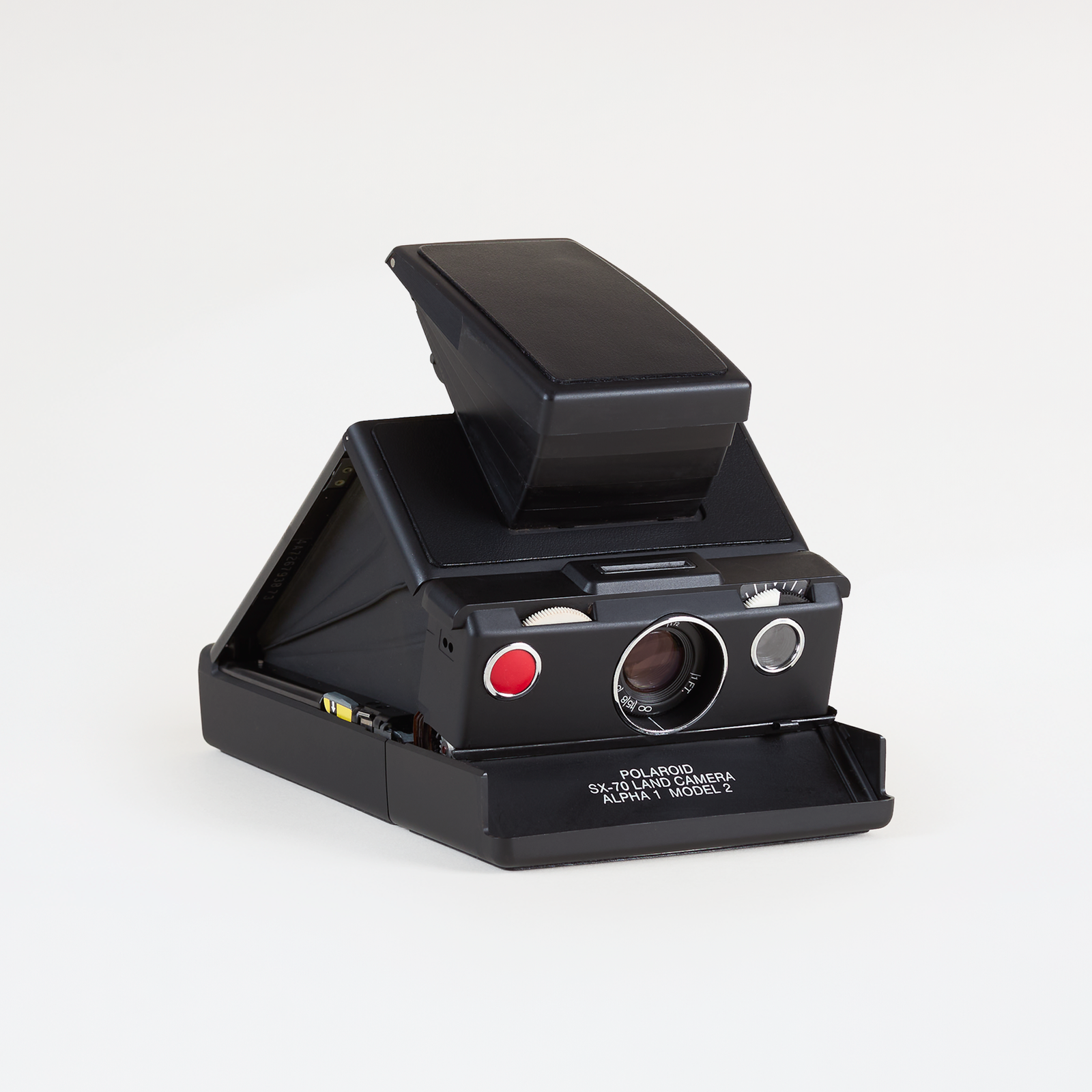 A vintage black Polaroid camera with its viewfinder open, featuring a red shutter button and white printed text on the base, photographed on a clean white background.