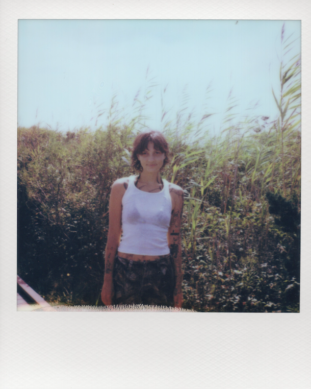 Polaroid-style photo of a person standing outdoors with greenery in the background